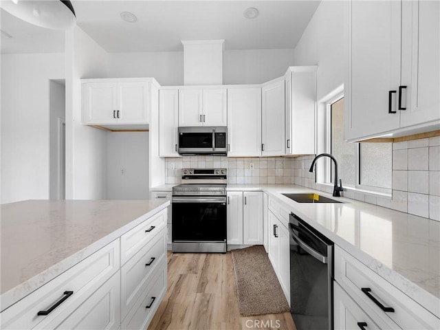 kitchen featuring appliances with stainless steel finishes, a sink, light stone counters, white cabinets, and light wood finished floors