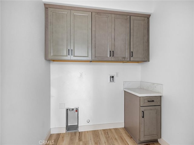 clothes washing area featuring gas dryer hookup, washer hookup, cabinet space, baseboards, and light wood finished floors