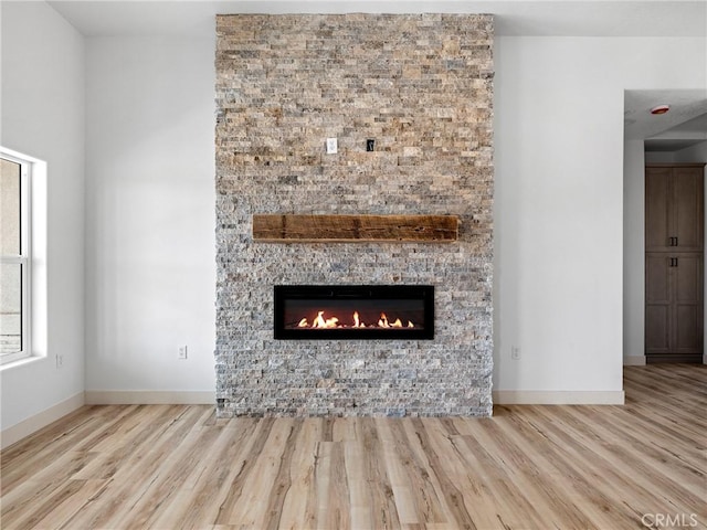 interior details with baseboards, a stone fireplace, and wood finished floors