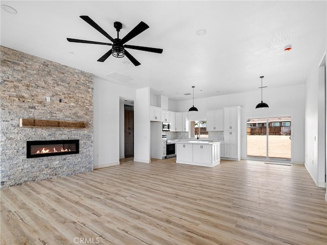 unfurnished living room with ceiling fan, a sink, a fireplace, light wood-style flooring, and baseboards