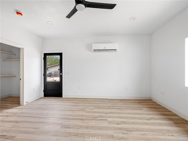 interior space featuring a walk in closet, baseboards, a wall unit AC, and light wood-style flooring