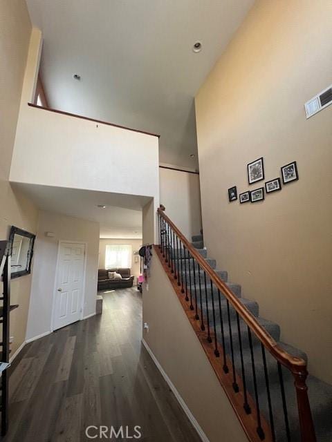 stairs featuring baseboards, a high ceiling, wood finished floors, and visible vents