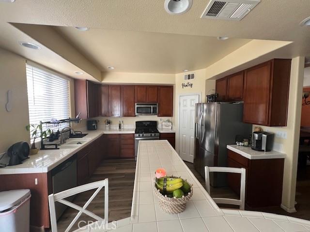 kitchen featuring tile counters, a sink, visible vents, and stainless steel appliances