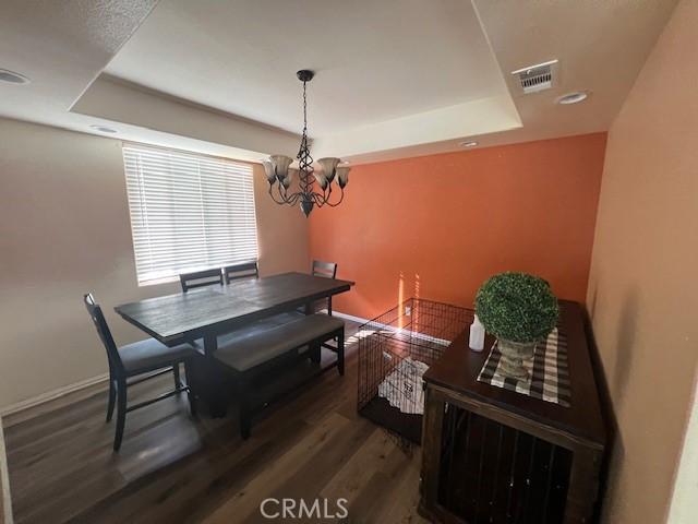 dining area featuring visible vents, a raised ceiling, wood finished floors, and an inviting chandelier