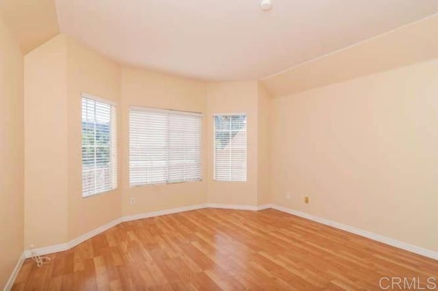 unfurnished room featuring baseboards, wood finished floors, and lofted ceiling