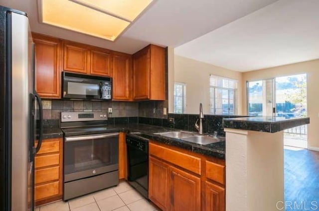 kitchen featuring a healthy amount of sunlight, brown cabinetry, a sink, and black appliances