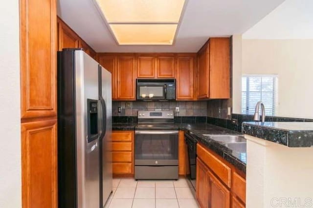 kitchen with backsplash, brown cabinets, light tile patterned floors, a sink, and black appliances