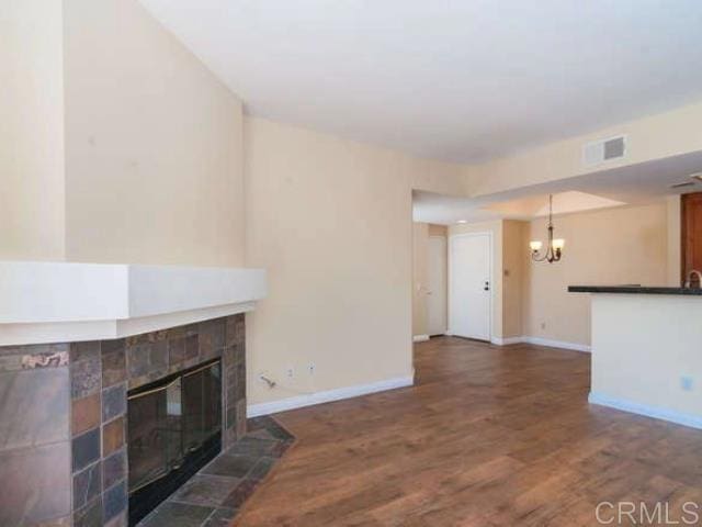 unfurnished living room with a notable chandelier, baseboards, wood finished floors, a tile fireplace, and visible vents
