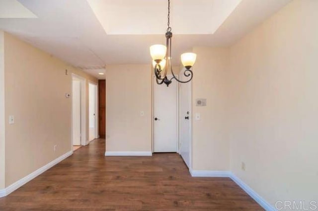 unfurnished dining area featuring baseboards, wood finished floors, and a notable chandelier
