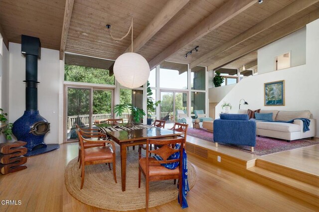 dining room with wood ceiling, beam ceiling, wood finished floors, high vaulted ceiling, and a wood stove