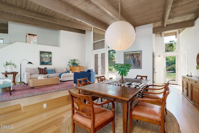 dining area with beam ceiling, wooden ceiling, light wood-style floors, and a high ceiling