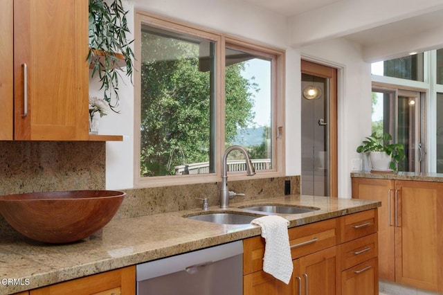 kitchen with a sink, stainless steel dishwasher, and light stone countertops