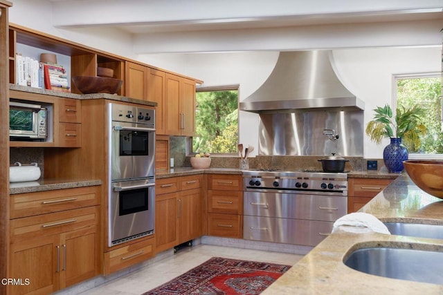 kitchen featuring stainless steel appliances, wall chimney exhaust hood, open shelves, light stone countertops, and decorative backsplash