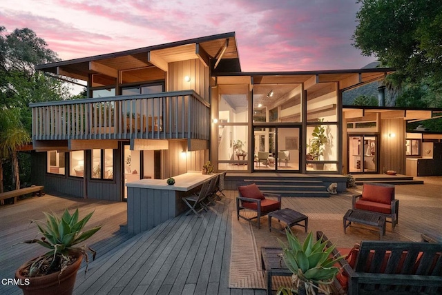 back of house at dusk featuring a wooden deck, a balcony, and outdoor lounge area