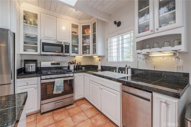 kitchen with appliances with stainless steel finishes, a sink, wooden ceiling, white cabinets, and light tile patterned flooring