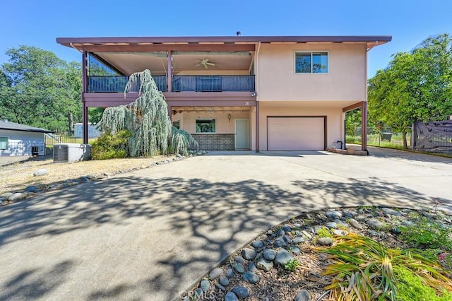 view of front of house featuring fence, a garage, central AC unit, a balcony, and driveway