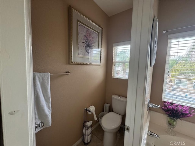 bathroom with toilet, baseboards, a healthy amount of sunlight, and a garden tub