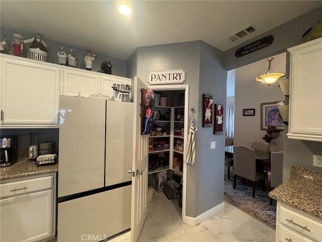 kitchen featuring visible vents, light stone countertops, white cabinets, freestanding refrigerator, and marble finish floor