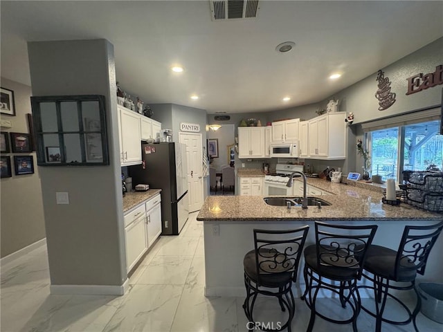 kitchen with a sink, marble finish floor, a peninsula, and white appliances