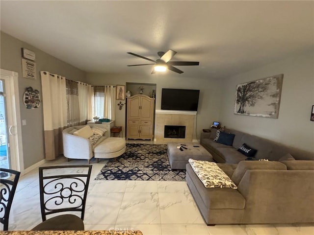 living room featuring a ceiling fan, a tiled fireplace, and marble finish floor