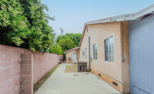 view of side of home with fence, stucco siding, a patio area, and crawl space
