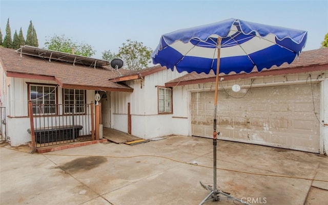 rear view of house featuring a shingled roof, an attached garage, concrete driveway, and a patio area