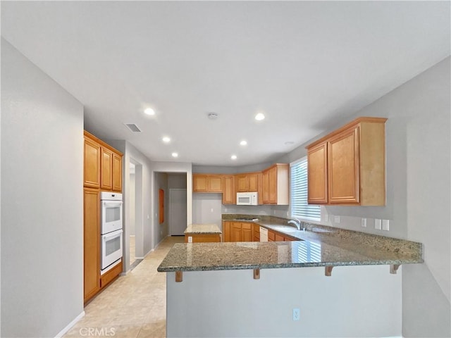 kitchen with visible vents, a peninsula, stone counters, recessed lighting, and white appliances