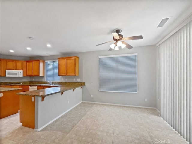 kitchen with a sink, white appliances, a breakfast bar area, a peninsula, and visible vents