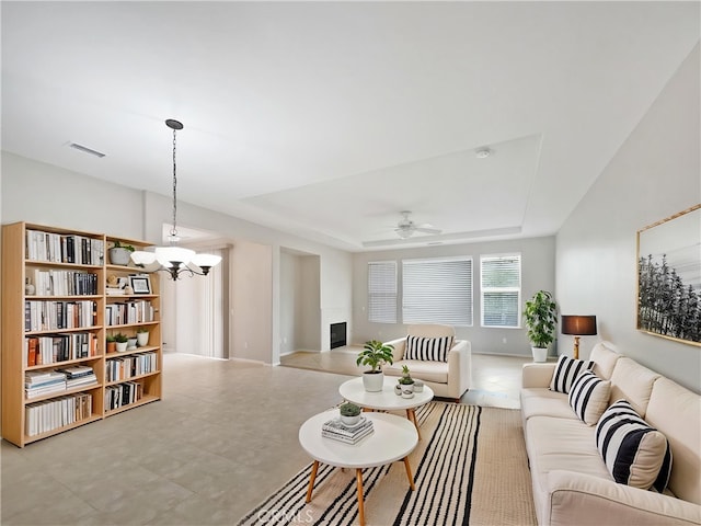 living area with a tray ceiling, a fireplace with raised hearth, ceiling fan with notable chandelier, and visible vents