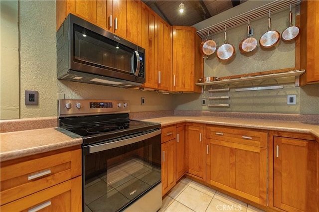 kitchen featuring light tile patterned floors, brown cabinets, light countertops, appliances with stainless steel finishes, and a textured wall