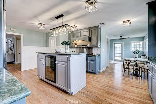 kitchen with ceiling fan, wainscoting, beverage cooler, gray cabinets, and light wood-style flooring