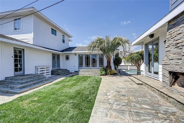 rear view of property featuring french doors, a patio, stucco siding, and a lawn