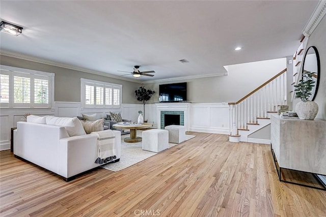 living area with stairs, ceiling fan, ornamental molding, and light wood finished floors