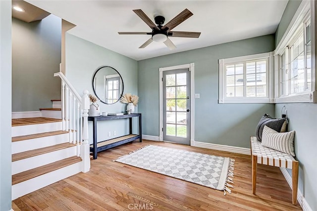 entryway featuring baseboards, a ceiling fan, light wood-style flooring, and stairs
