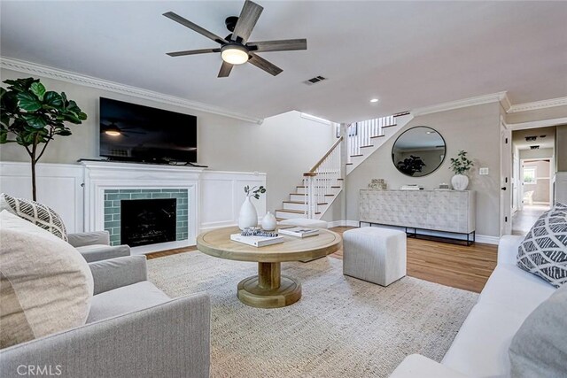 living area featuring ornamental molding, wood finished floors, stairway, a tile fireplace, and a ceiling fan