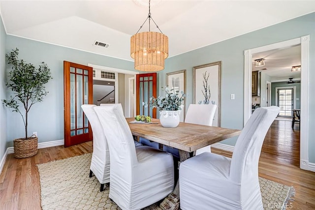 dining area with visible vents, vaulted ceiling, wood finished floors, baseboards, and a chandelier