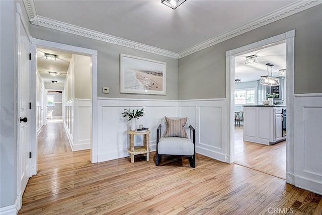 sitting room featuring a wainscoted wall, ornamental molding, a decorative wall, and light wood-style flooring