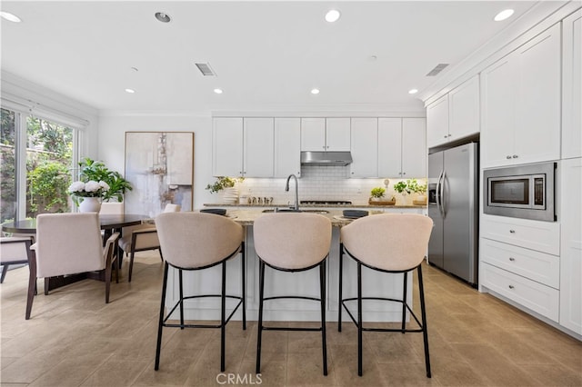 kitchen with appliances with stainless steel finishes, a sink, an island with sink, under cabinet range hood, and visible vents