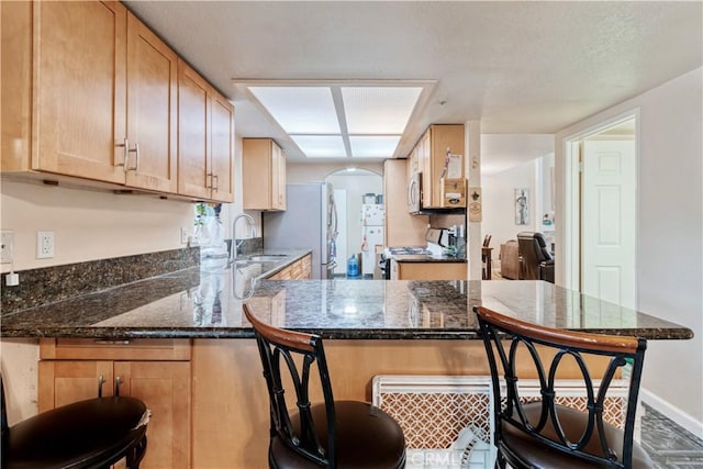 kitchen with stainless steel appliances, a sink, arched walkways, a peninsula, and a breakfast bar