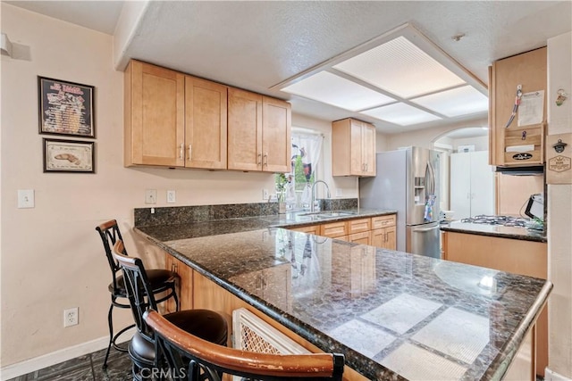 kitchen featuring a sink, stainless steel fridge, a peninsula, baseboards, and a breakfast bar area