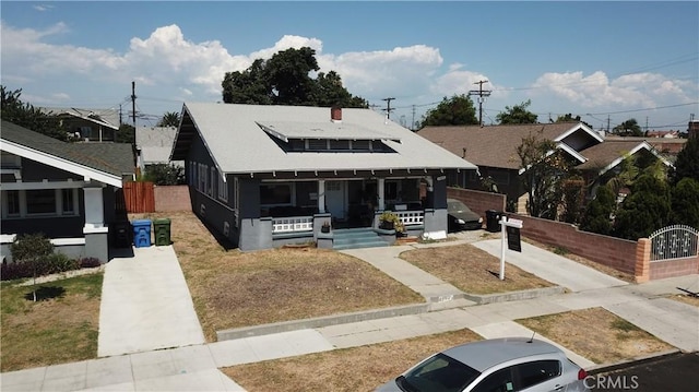 bungalow featuring a porch, driveway, fence, and roof mounted solar panels