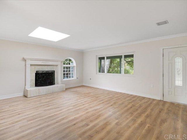 unfurnished living room with a skylight, ornamental molding, baseboards, and light wood finished floors