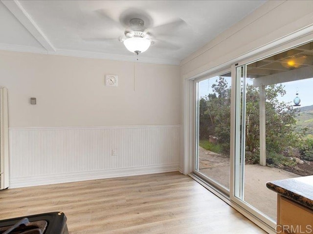 unfurnished dining area featuring a ceiling fan, light wood finished floors, a wainscoted wall, and ornamental molding