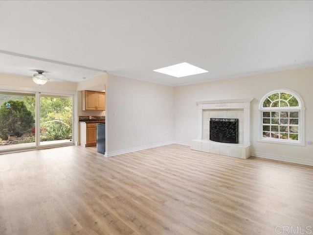 unfurnished living room featuring a skylight, baseboards, plenty of natural light, and light wood finished floors
