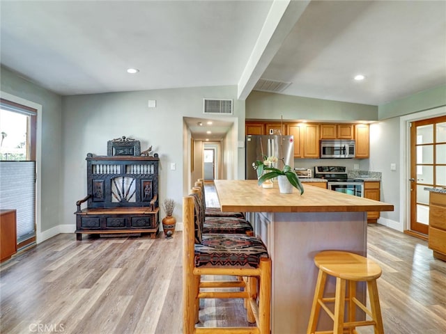 kitchen with a breakfast bar, stainless steel appliances, vaulted ceiling with beams, visible vents, and butcher block countertops