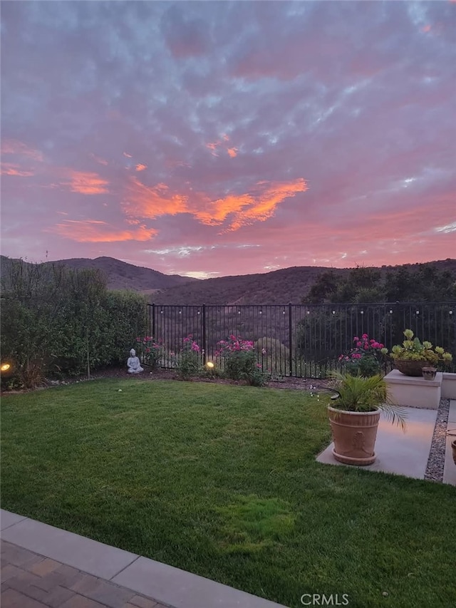 yard at dusk with a mountain view and fence