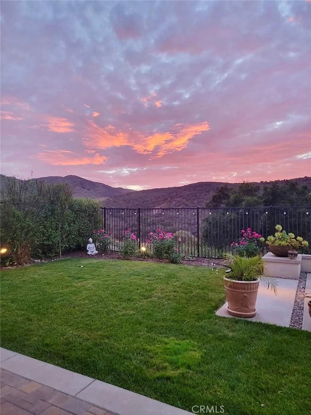 yard at dusk featuring a mountain view and fence