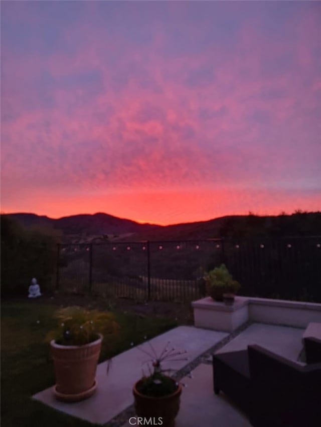 patio terrace at dusk with fence, a mountain view, and an outdoor hangout area