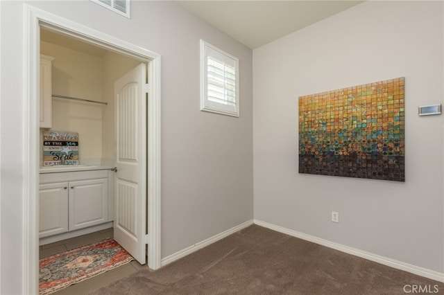 hall featuring visible vents, baseboards, dark carpet, and a sink