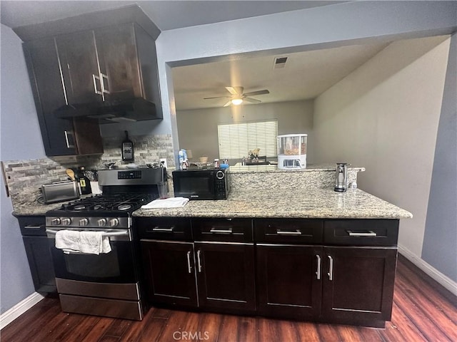 kitchen featuring dark wood-style flooring, a peninsula, black microwave, backsplash, and gas stove